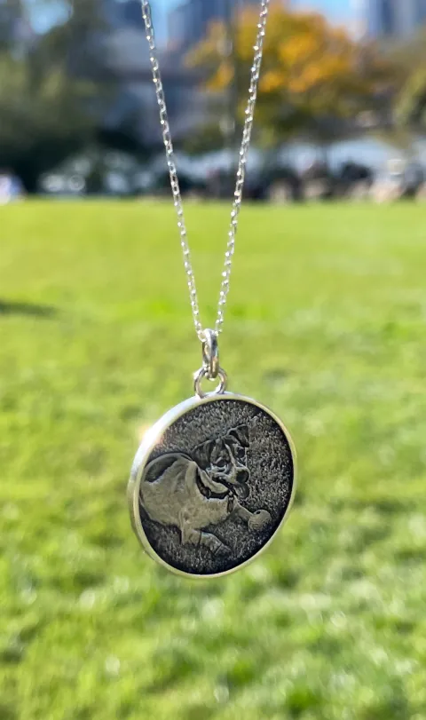 Custom dog portrait pendant photographed in a city park